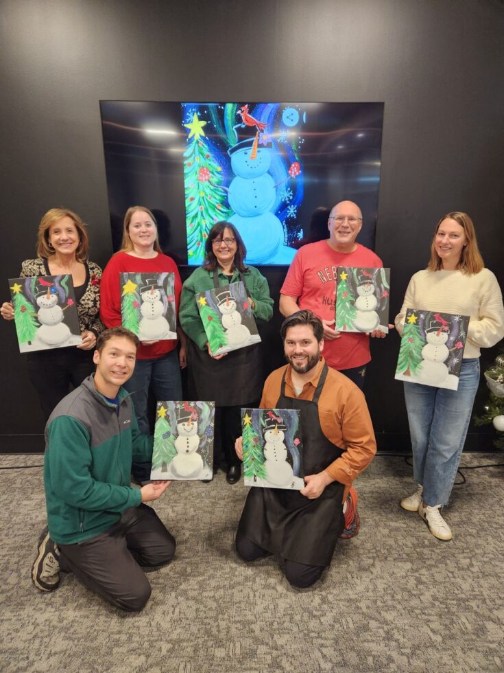 Group of seven people holding up their artwork and smiling indoors.